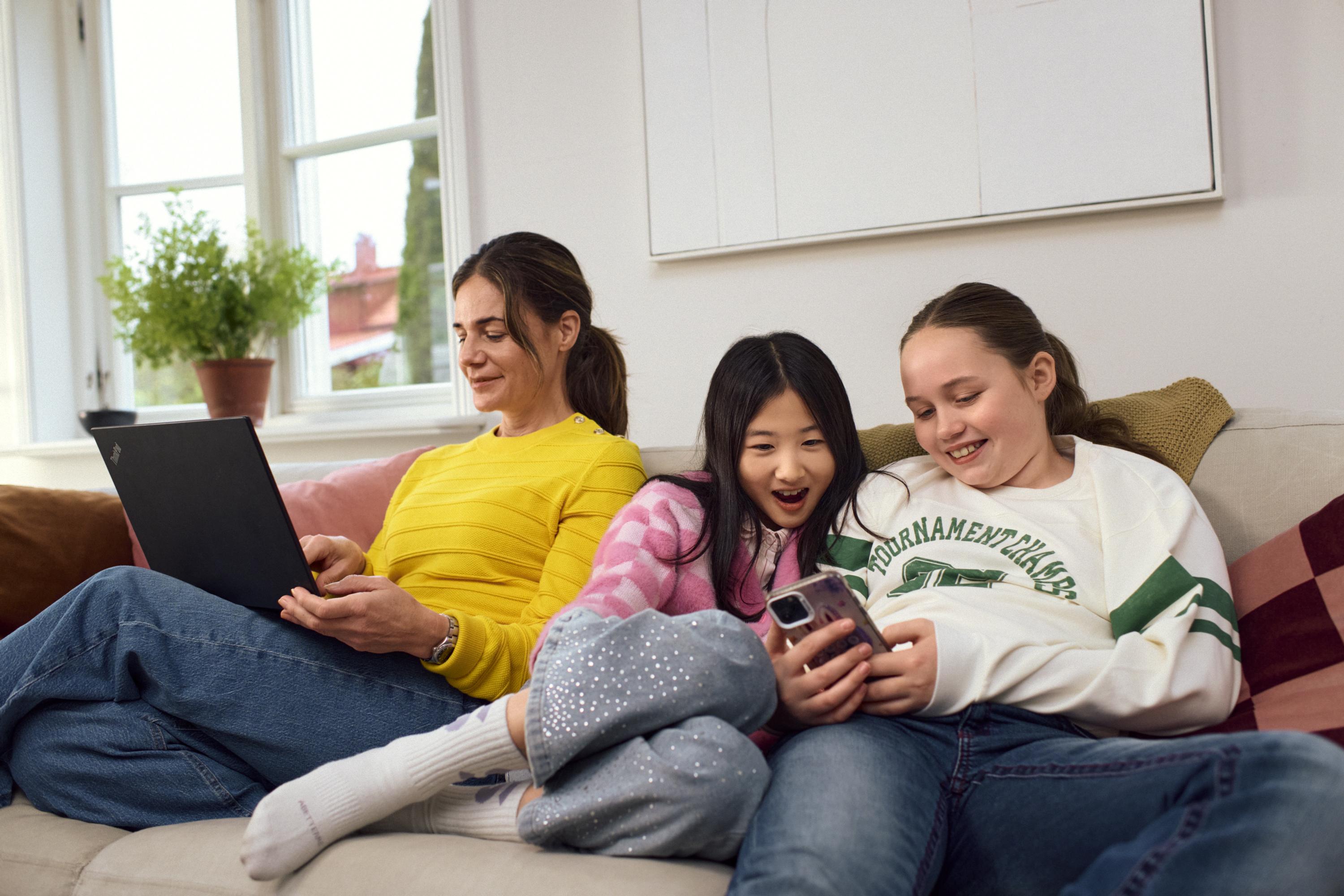 Unga tjejer tittar i mobilen tillsammans i soffan