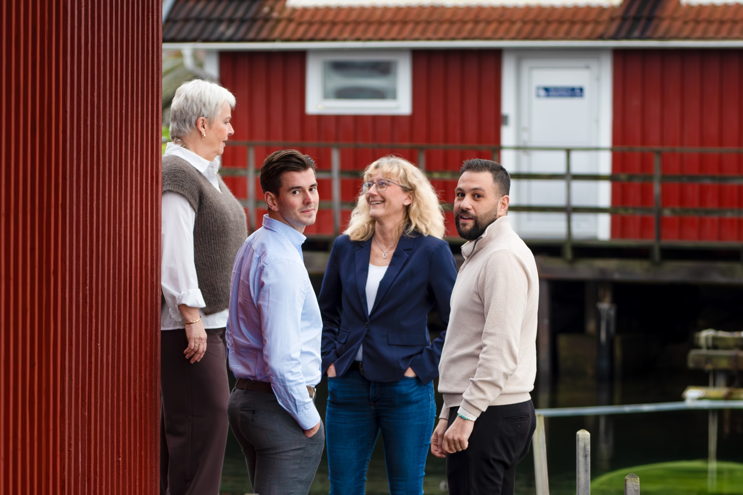 gruppfoto fyra pers, utomhus bland röda bodar
